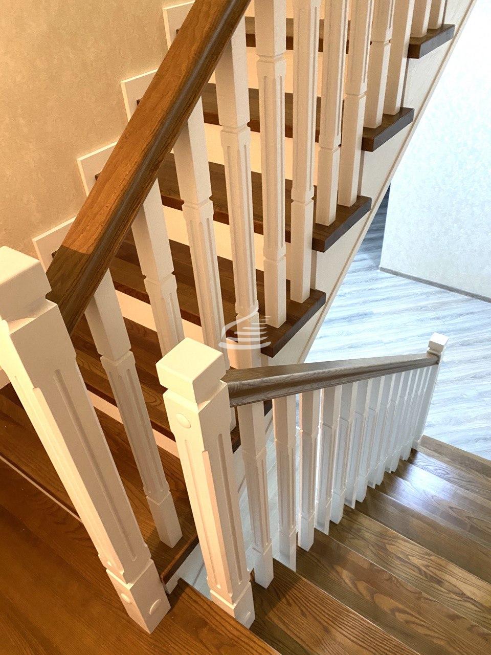 Изящная лестница в современном классическом стиле из массива Ясеня.  Подиумная ступень необычной формы смотрится свежо и актуально, а ограждение в виде прямых столбов с фрезеровкой и решётчатая дверь придает этой лестнице легкость и изящество.
